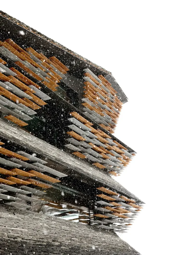 Detail der Haus-Balma-Fassade aus Stein- und Holzlamellen im Schneefall